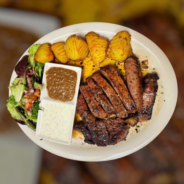 Grilled steak slices, roasted potatoes, and a side salad with two sauces on a white plate.