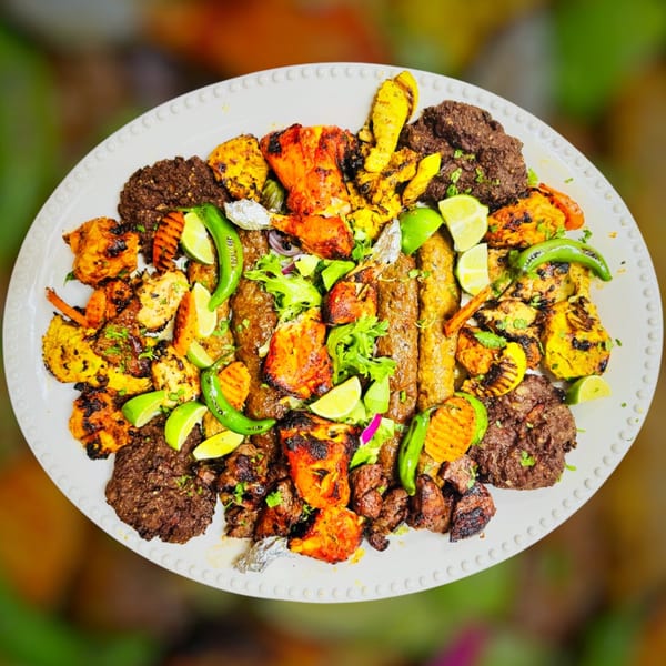 A large platter of Maza Grill's halal mixed grill, featuring various grilled meats, vegetables, and limes.