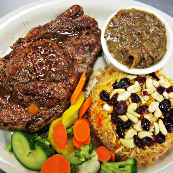 Halal steak with gravy, colorful rice pilaf topped with cashews and cranberries, and steamed vegetables.
