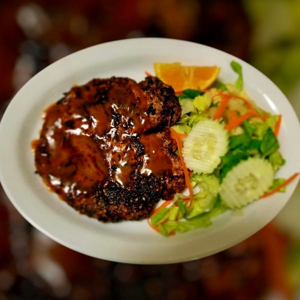 Halal grilled meat with a glossy sauce, served with a fresh green salad and an orange slice.