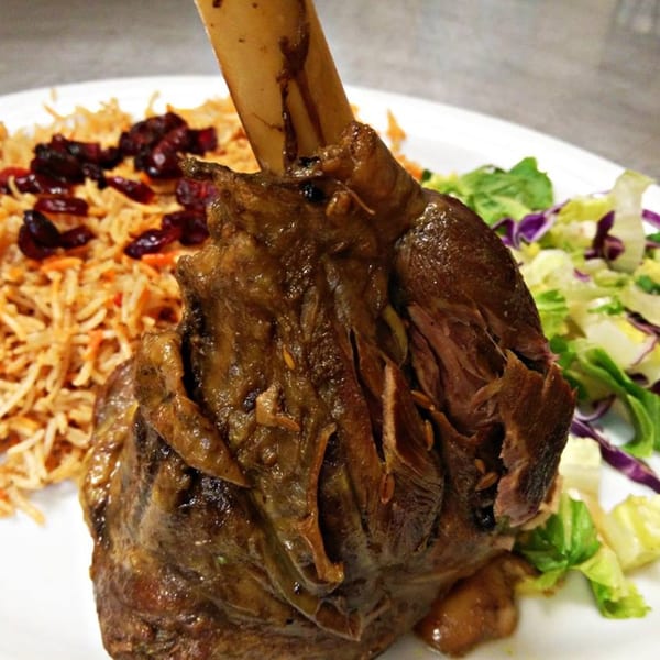 Halal lamb shank with rice, cranberries, and a side salad on a white plate at Maza Grill.