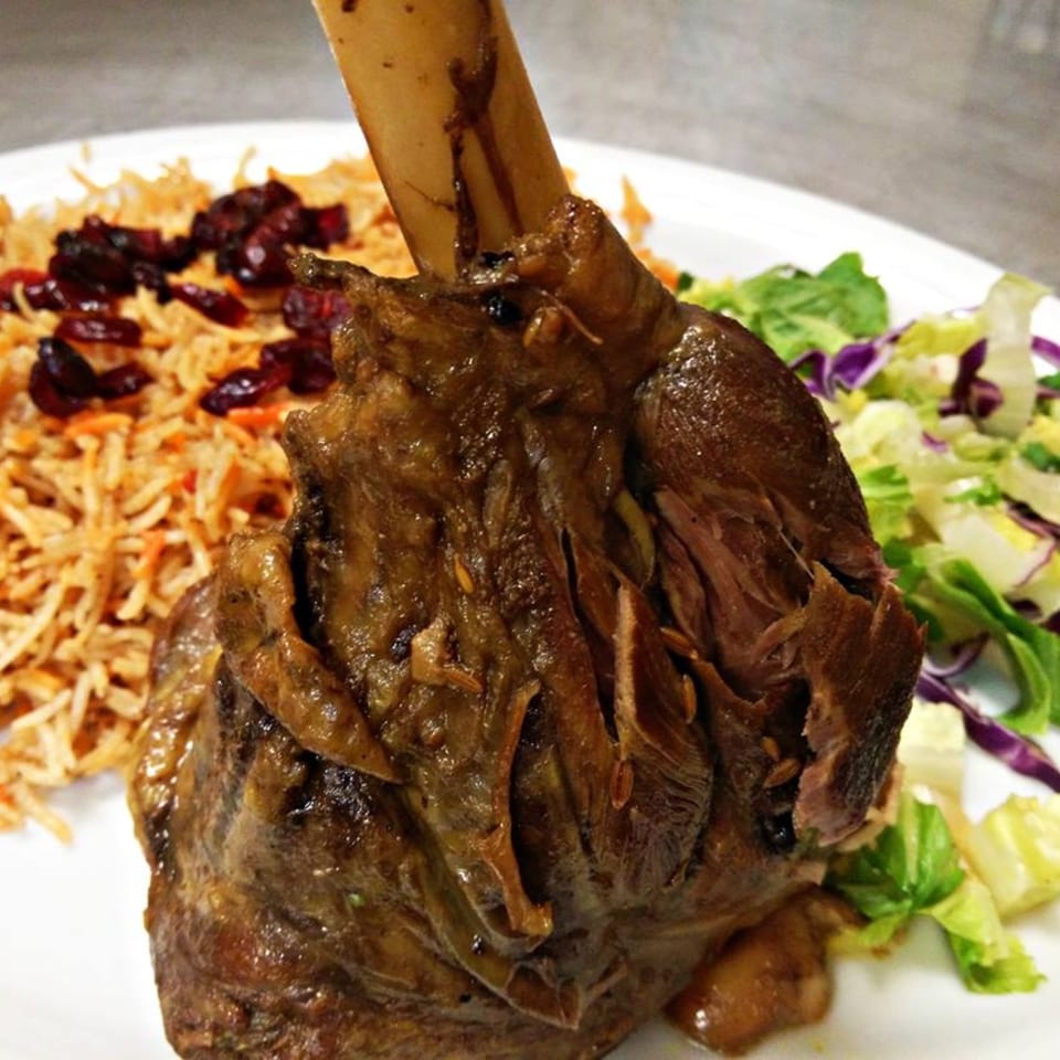 Halal lamb shank with rice, cranberries, and a side salad on a white plate at Maza Grill.